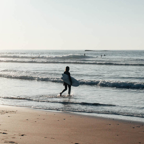 Laurenz Steierl läuft mit Surfbrett ins Wasser am Praia Amado