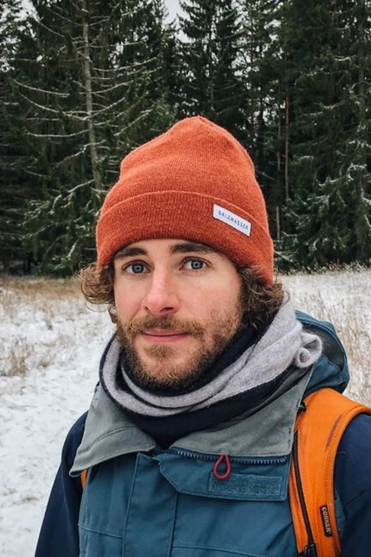Mann trägt nachhaltige SALZWASSER Mütze in Rostrot im Wald im Winter