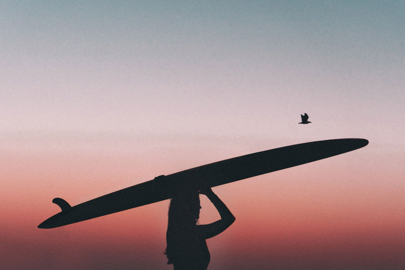 Frau mit Surfbrett vor rotem Sonnenuntergang