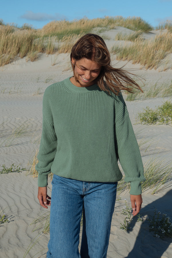 Frau trägt nachhaltigen Strickpullover von SALZWASSER in Grün am Strand
